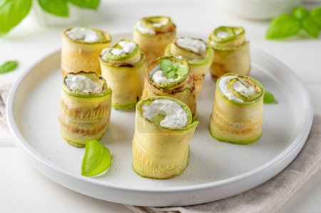 Zucchini-Vorspeisenrollen mit Frischkäse, Knoblauch und Kräutern auf einem Teller auf weißem Holzgrund. Selektiver Fokus