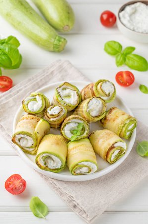 Photo for Zucchini appetizer rolls with cream cheese, garlic and herbs on a plate on a white wooden background. Selective focus - Royalty Free Image