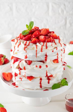 Téléchargez les photos : Pavlova gâteau stratifié avec des fraises fraîches, sauce et crème fouettée sur un fond en bois blanc. Beau gâteau d'été. Concentration sélective - en image libre de droit