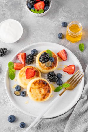 Photo for Cottage cheese pancakes, syrniki, ricotta fritters with fresh berries, honey and sour cream on a gray concrete background. Healthy and delicious breakfast. Top view, copy space - Royalty Free Image