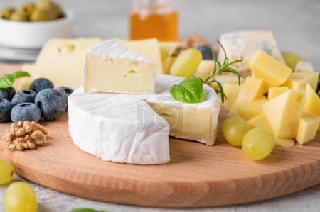 Cheese plate with a variety of cheeses, honey, grapes, nuts, olives, blueberries and fresh herbs on a concrete background. A festive snack. Top view, copy space.
