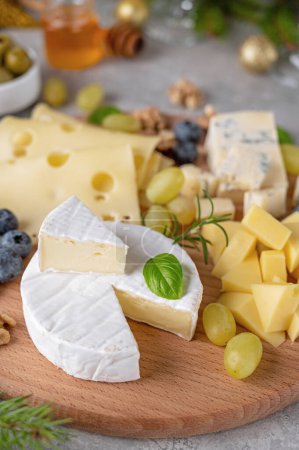 Cheese plate with a variety of cheeses, honey, grapes, nuts, olives, blueberries and fresh herbs on a concrete background. Festive Christmas and New Year's snack. Top view, copy space.