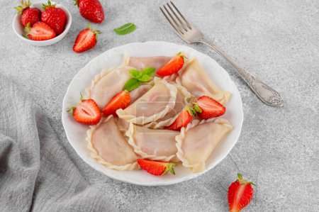 Tasty traditional dumplings, varenyky or pierogi with strawberry and sour cream on a white plate