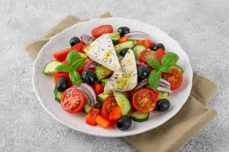 Ensalada griega de verduras frescas jugosas, queso feta, hierbas y aceitunas en un plato blanco sobre un fondo de hormigón ligero. Comida saludable. Copiar espacio, vista superior