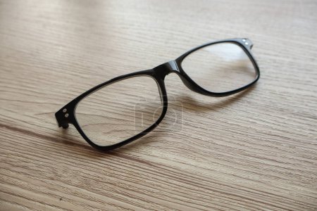 A pair of broken reading glasses without temples, placed on a table. The damage to the glasses is evident, showcasing the wear and tear from daily use