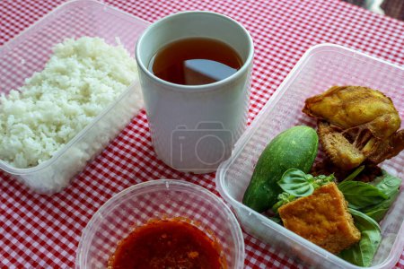 Traditional Indonesian meal featuring fried chicken, tofu, tempeh, fresh vegetables, white rice, sambal pecel, and unsweetened tea