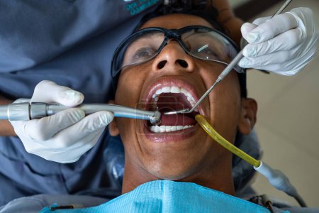 Foto de Paciente masculino visita consultorio dental. Dentista con guantes protectores de goma realiza tratamiento dental. - Imagen libre de derechos