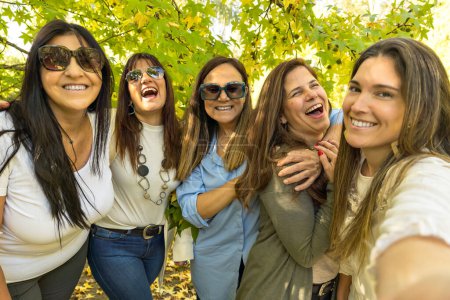 Foto de Un grupo de cinco mujeres animadas se están tomando un selfie en un día soleado con un árbol frondoso en el fondo. Selfie con amigos. - Imagen libre de derechos