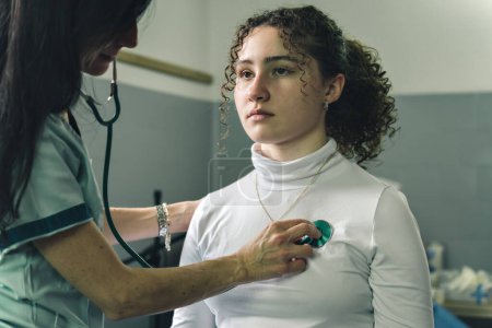Foto de Mujer joven en el consultorio del médico, tomando su ritmo cardíaco con estetoscopio. - Imagen libre de derechos