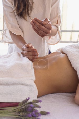 Foto de Primer plano del terapeuta femenino aplicando aceite de masaje en las manos antes de la terapia sobre la dama acostada en la mesa de masaje. - Imagen libre de derechos