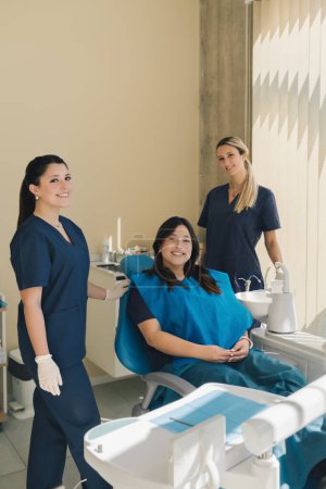 Foto de Retrato de tres mujeres, dentista, asistente y paciente en un consultorio dental sonriendo y mirando a la cámara. Concepto de salud dental. - Imagen libre de derechos