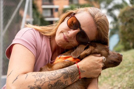 Foto de Primer plano de una mujer con los ojos cerrados y gafas de sol abrazando a su perro cariñosamente. - Imagen libre de derechos