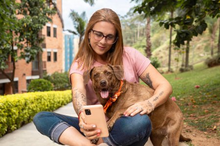 Foto de Mujer sentada con gafas de lectura tomando una selfie con su mascota sentada en el parque. - Imagen libre de derechos