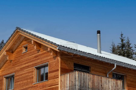 Holzhaus mit Edelstahlkamin und dünner Schneedecke auf dem Dach