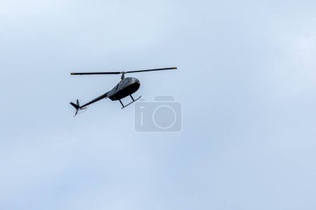 A black helicopter crosses the blue sky with clouds. Transportation. Urban. Trip