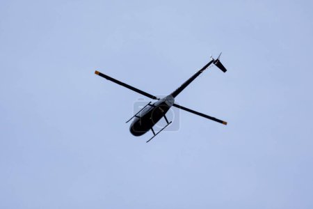 A black helicopter crosses the blue sky with clouds. Transportation. Urban.
