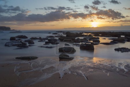 Téléchargez les photos : Longue exposition à l'océan avec de l'eau laiteuse et aux rochers au lever du soleil avec soleil à Spoon Bay - en image libre de droit