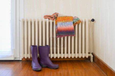 Photo for Boots, hat and scarf drying on a cast-iron radiator - Royalty Free Image