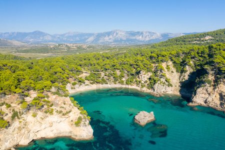 This landscape photo was taken, in Europe, in Greece, in Epirus, towards Igoumenitsa, at the edge of the Ionian Sea, in summer. We see the fine sandy beach of Alonaki Fanariou and its green rocky cliffs, under the sun.