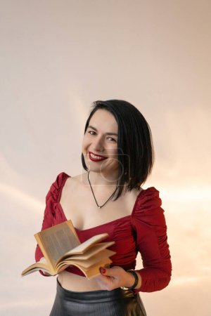 Téléchargez les photos : Une fille en chemise rouge avec une coupe de cheveux courte tient un livre dans ses mains - en image libre de droit