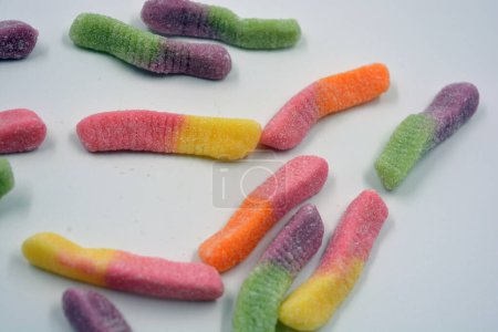 Photo for Beautiful and bright colored sweets of children's candies in the form of sweet earthworms of different colors arranged on a white matte background. - Royalty Free Image
