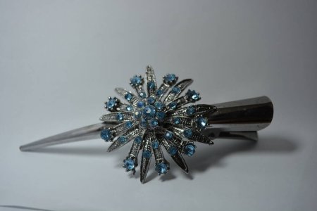 Beautiful women's jewelry, steel and elegant costume jewelry. Grey metal hair clip with large metal flower made of blue stones set on white background.