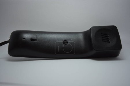 A black plastic handset from a landline phone without buttons is located on a white background.