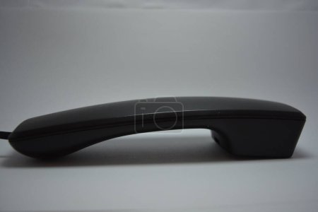 A black plastic handset from a landline phone without buttons is located on a white background.