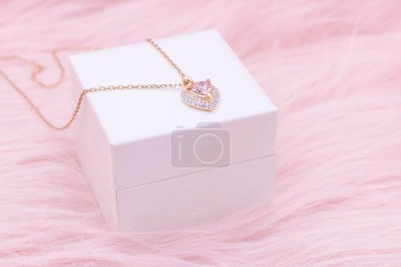Téléchargez les photos : Necklace jewelry, Close up of a heart shape gemstone with a gold chain necklace on pink background. An elegant necklace for valentine's day. - en image libre de droit
