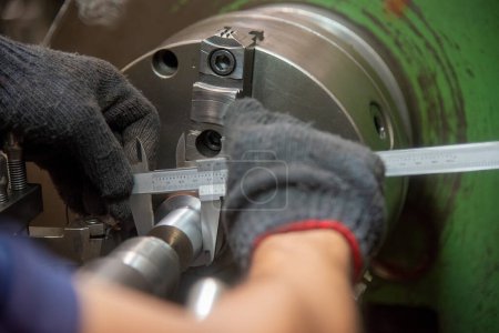 Nahaufnahme des Bedieners, der mit dem Vernier-Bremssattel Teile der Metallwelle im Außendurchmesser misst. Die Qualitätskontrolle auf der Drehmaschine. 