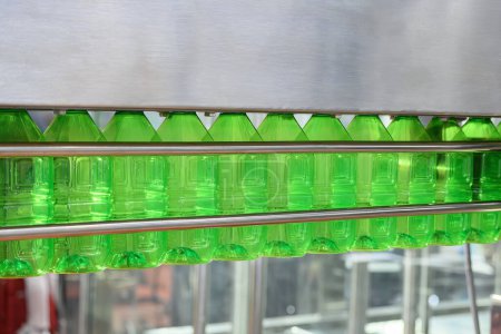 Foto de Las botellas vacías de agua potable verde que cuelgan de la cinta transportadora para el proceso de llenado. La alta tecnología del proceso de fabricación de agua potable. - Imagen libre de derechos