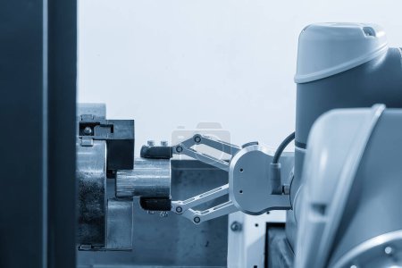 El brazo robótico automático que agarra las piezas metálicas de la máquina de torno CNC. El proceso de manipulación de materiales de alta tecnología por sistema robótico en la máquina de torneado. 