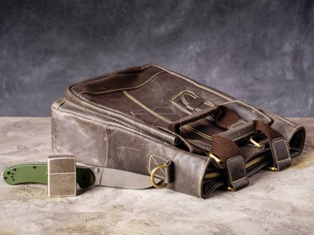 Foto de Green folding EDC knife and silver lighter near a leather business casual bag - Imagen libre de derechos
