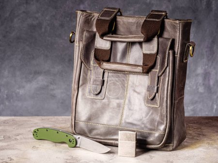 Foto de Green folding EDC knife and vintage lighter near a leather business casual bag - Imagen libre de derechos
