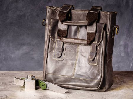 Foto de Green folding EDC knife and vintage lighter near a leather casual bag - Imagen libre de derechos