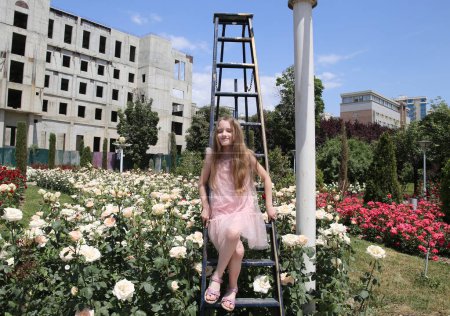 Foto de Niña sentada en una escalera entre rosas blancas - Imagen libre de derechos