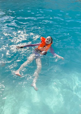 Foto de Niña vistiendo chaleco vivo nadando en el mar junto a un velero - Imagen libre de derechos