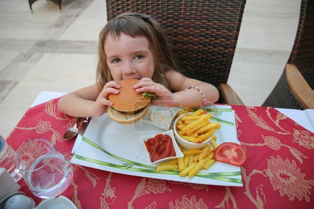Ein kleines Mädchen mit Appetit isst einen Burger