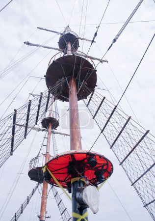 Wooden top of the sailing ship mast, yards and rigging against cloudy sky