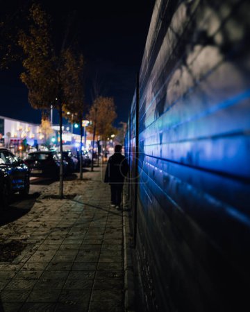 Téléchargez les photos : Réflexions lumineuses d'urgence la nuit dans le mur. Garçon marchant dans l'obscurité vers le centre commercial avec des lumières d'urgence. - en image libre de droit