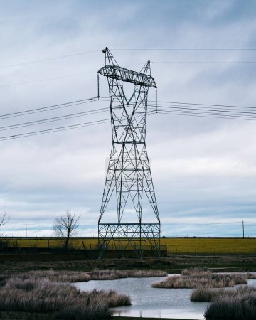 Foto de High voltage post or High voltage tower in the countryside with a small lake. Cloudy background. - Imagen libre de derechos