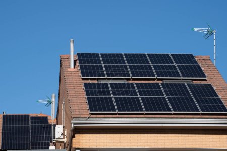 Foto de Solar photovoltaic panels on neighbourhood house roof against blue sky. - Imagen libre de derechos