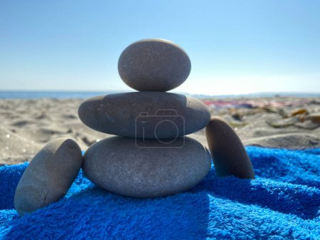 Téléchargez les photos : Gros plan de Apacheta Stone Mound avec la forme de l'homme sur la plage de sable fin et ensoleillée om dessus de serviette bleue. Équilibre de vie, harmonie et concept de paix - en image libre de droit