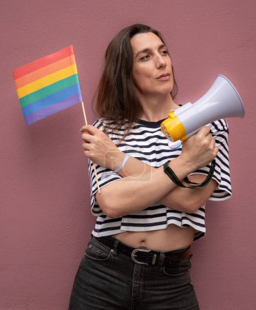 Transsexual woman looking away and holding a rainbow flag and a megaphone to support LGBTQ community as activist.