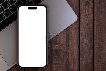 Foto de Mockup smartphone iPhone 14 Pro Max con pantalla blanca en blanco y Macbook en el fondo de madera. Apple es una empresa multinacional de tecnología. Batumi, Georgia - 26 de octubre de 2022 - Imagen libre de derechos