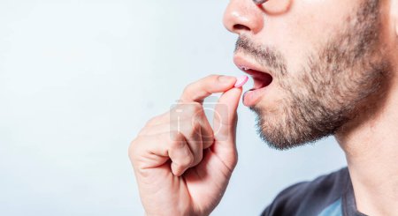 Close-up of a man taking an aspirin. Person taking a pill isolated, Close up of young man putting a pill in his mouth. Self-medication concept, Man putting a pill in his mouth isolated