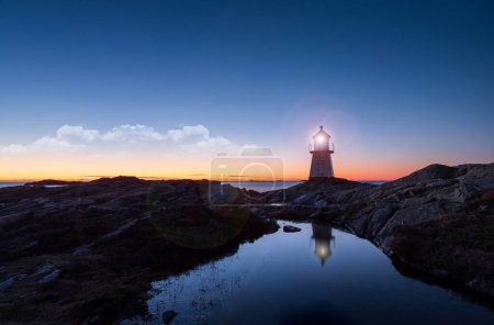 Photo for Lighthouse surrounded by rocks at night, lighthouse with lights on at sunset - Royalty Free Image