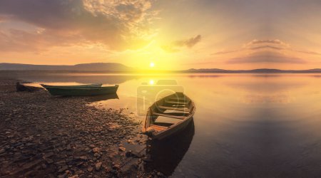 Wooden boats on the shore of a lake at sunset, small wooden boats parked on the shore of the lake, two wooden boats in the water at sunset