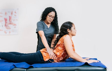 Young physiotherapist assisting female patient with lower back pain, Woman performing lumbar physiotherapy to patient. Physiotherapist assisting lumbar treatment to lying patient