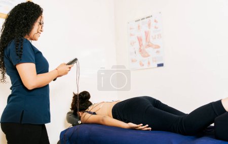 Photo for Professional physiotherapist electrostimulating a lying patient. Physiotherapist electrostimulating a patient. Lower back therapy with electrode pads. Electrode treatment to patient lying down - Royalty Free Image